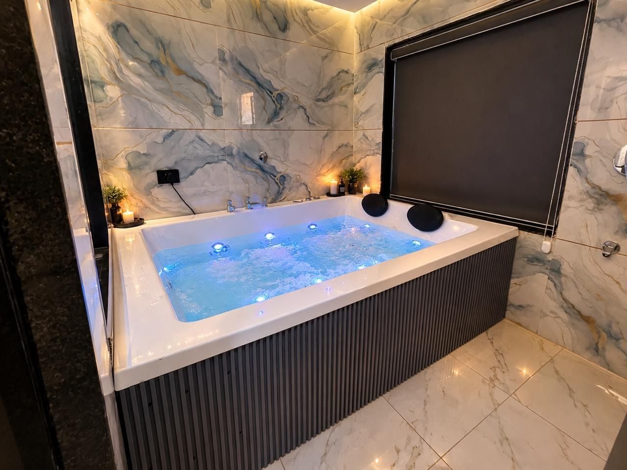 A modern bathroom with a marble wall, a large bathtub, and a black screen.