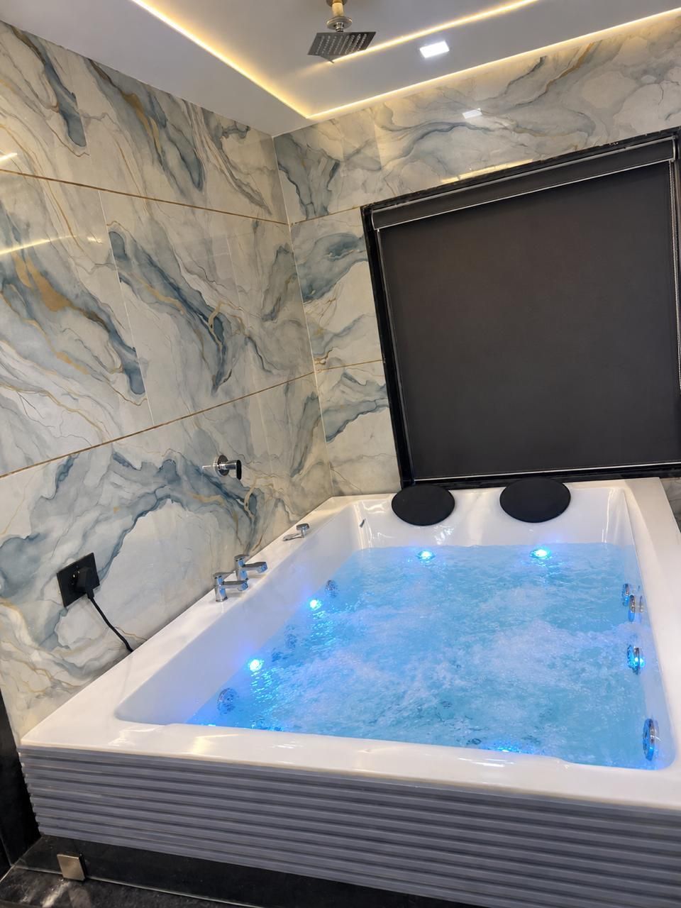 A modern bathroom with a marble wall, a bathtub with water jets, and a mounted television.