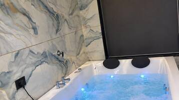 A modern bathroom with a marble wall, a bathtub with water jets, and a mounted television.