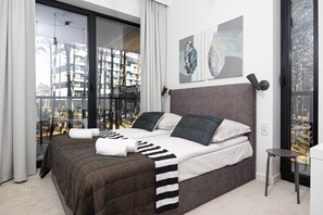 Ein modernes Schlafzimmer mit einem großen Bett, Blick auf die Stadt und einem kleinen Tisch.