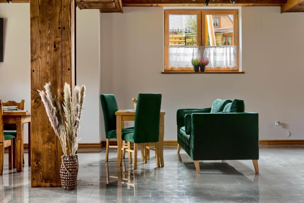 A room with a wooden dining table, green chairs, a green sofa, and a window with plants.