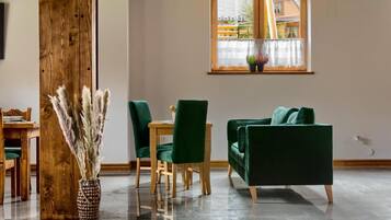 A room with a wooden dining table, green chairs, a green sofa, and a window with plants.