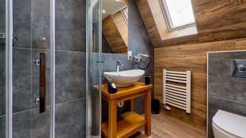 A modern bathroom with a glass shower enclosure, a wooden vanity with a sink, and a sloped ceiling with wooden paneling.