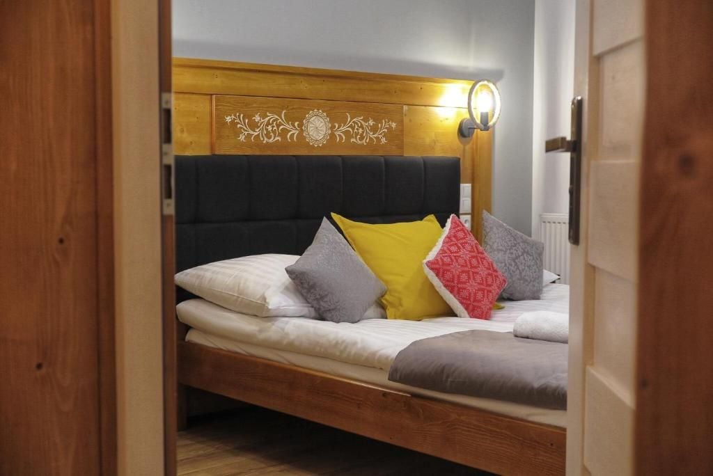 A single bed with a wooden headboard, multiple pillows, and a wall-mounted light fixture.