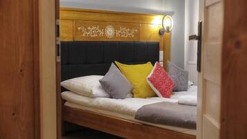 A single bed with a wooden headboard, multiple pillows, and a wall-mounted light fixture.