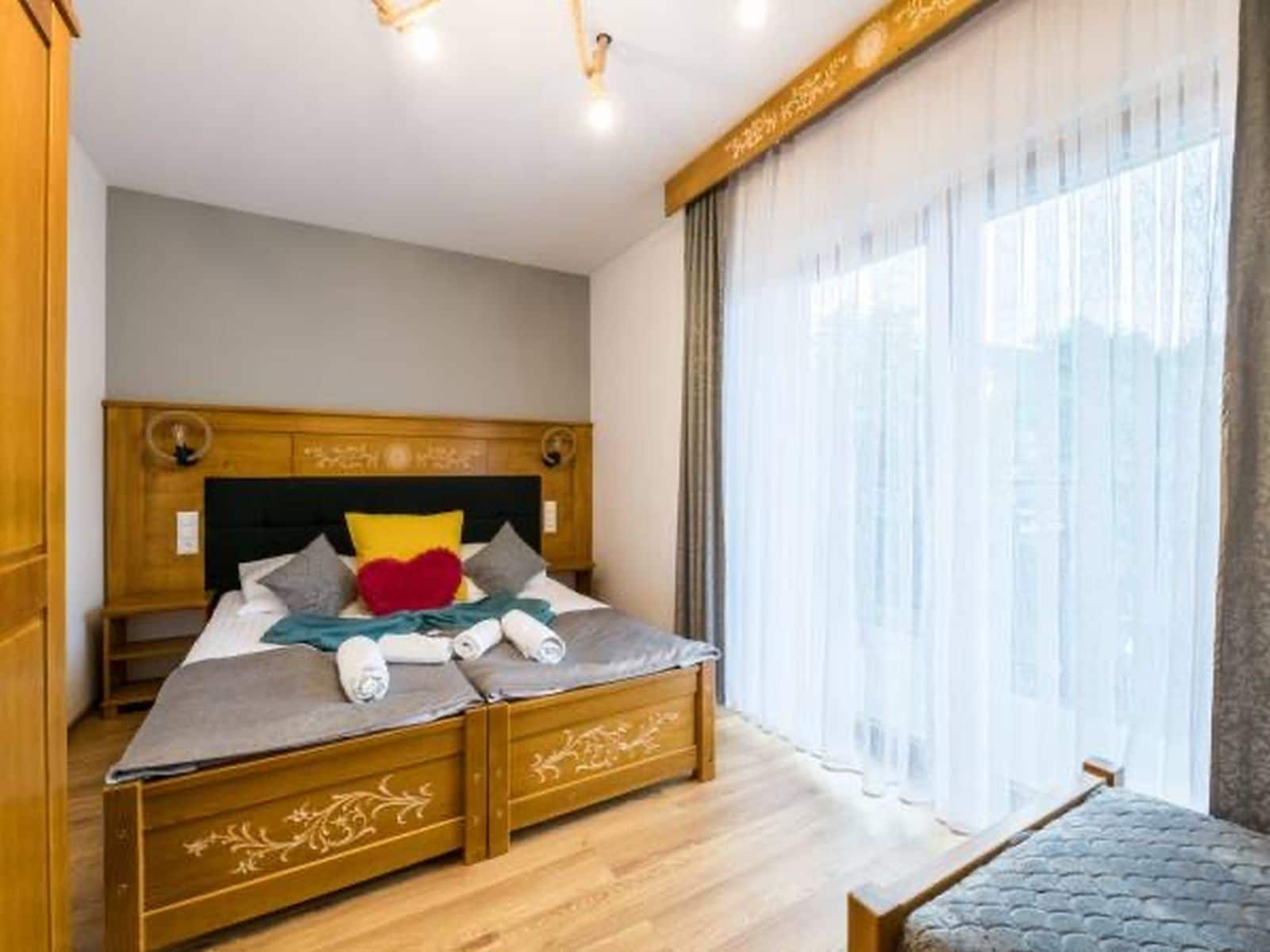 A bedroom with a wooden bed, a bench, and a large window with sheer curtains.