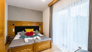 A bedroom with a wooden bed, a bench, and a large window with sheer curtains.