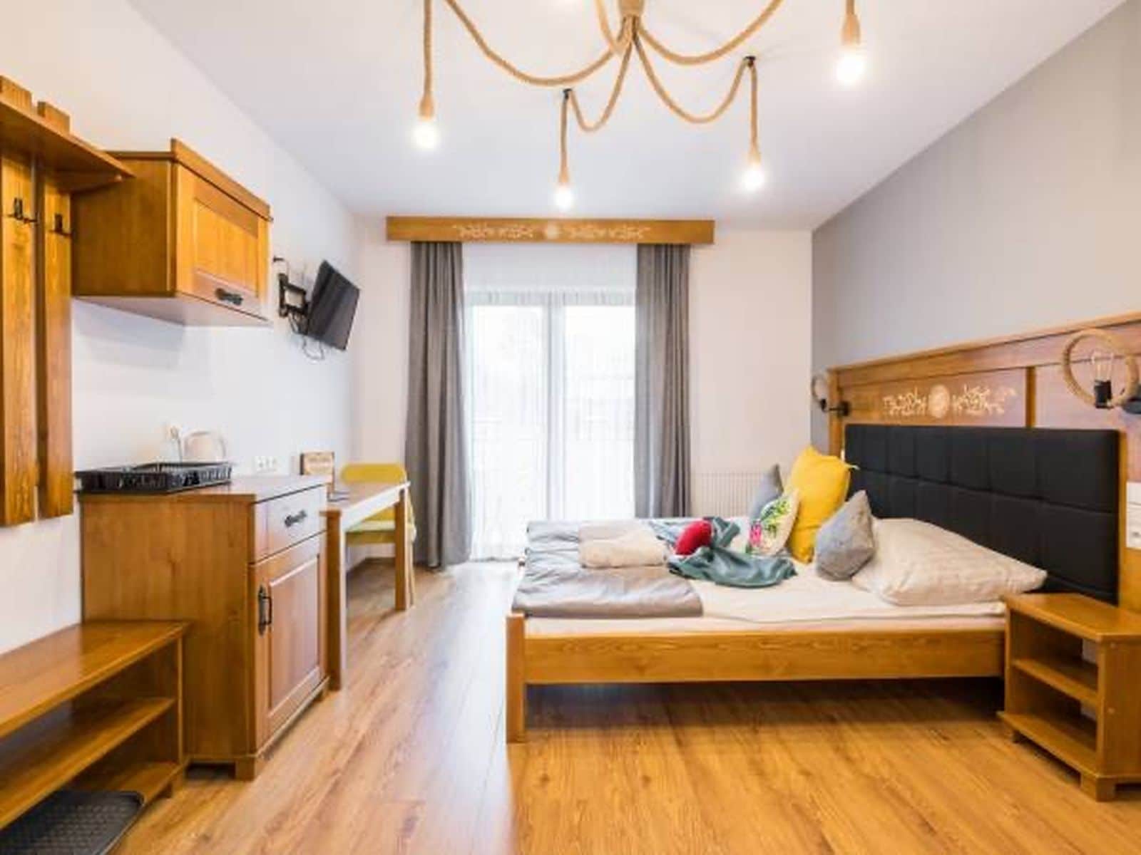 Un dormitorio con una cama, cabecera de madera, mesitas de noche, un escritorio y un televisor.