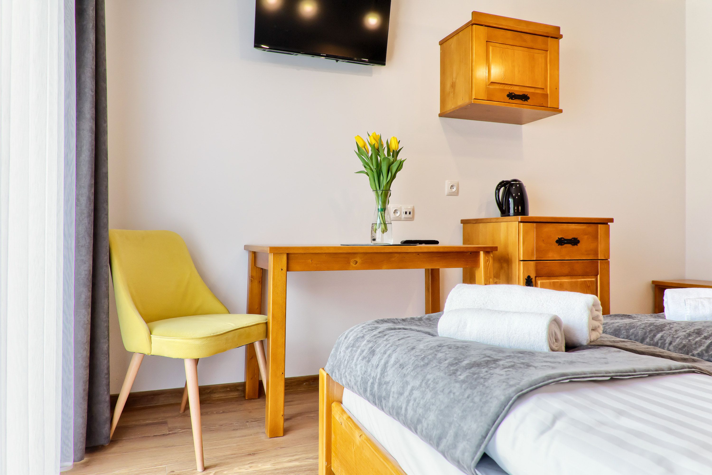 A hotel room with a bed, a desk, a chair, a TV, a wooden cabinet, and a vase with flowers.