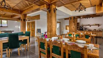 Ett rymligt matområde med träbord och stolar, ett kök i bakgrunden och ett högt trätak med hängande lampor.