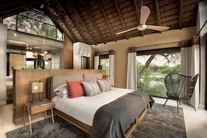 Een slaapkamer met een groot bed, een houten hoofdbord, een nachtkastje, een stoel en uitzicht op de omgeving.