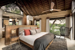 Un dormitorio con una cama grande, cabecera de madera, una mesita de noche, una silla y vistas al exterior.