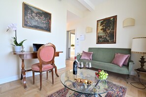 Ein Wohnzimmer mit einem Glastisch, einem grünen Sofa, einem Holzstuhl, einem Schreibtisch mit einem Laptop und zwei Bildern an der Wand.