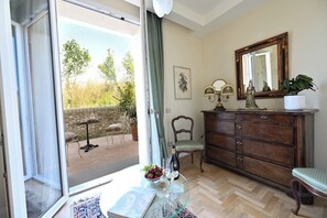 Una habitación con puerta corredera de vidrio que da a un espacio exterior con una mesa lista para dos personas, un aparador de madera con un espejo y una estatua encima.