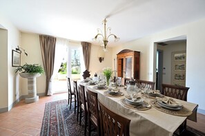 Ein Esszimmer mit einem langen Tisch, der für eine Mahlzeit gedeckt ist, einer Chandelier und Blick durch eine Glastür.