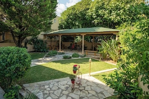 A covered outdoor seating area with a stone patio, surrounded by lush greenery and a small garden. - Konstantinos Hotel (Lefkada)