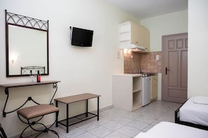 Habitación de hotel compacta con cama, una mesita, una silla, televisión, kitchenette y baño.