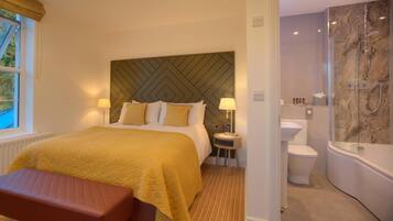 A hotel room with a large bed, bedside lamps, a bench, a bathroom with a bathtub, toilet, and sink.