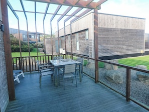 A covered outdoor area with a table and chairs, wooden deck, and a view of a building with a wooden facade. - 74 Porthmeor (Redruth)