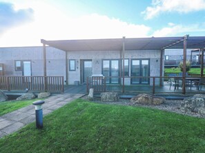 A building with a covered outdoor seating area, a wooden deck, and a grassy lawn. - 74 Porthmeor (Redruth)