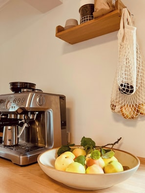 Ett kök med en kaffemaskin, en skål med frukt och en hängande väska.