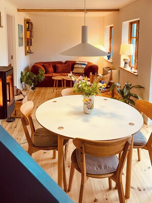 Ein gemütliches Wohnzimmer mit einem runden Esstisch, Holzsesseln, einer Couch und einem Bücherregal.