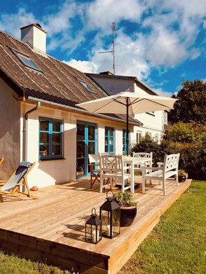 Et hus med en træterrasse, udendørs møbler og en stor parasol.