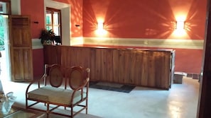 A reception area with a wooden reception desk, two wall-mounted lights, a wooden chair, and a door leading to another room. - Hacienda San Francisco Tzacalha (Dzidzantun)