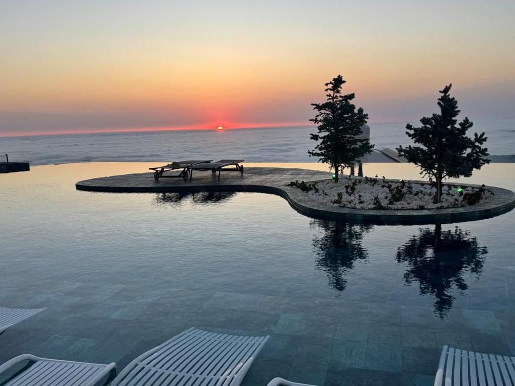 A infinity pool with lounge chairs, a small island with trees, and a sunset view.