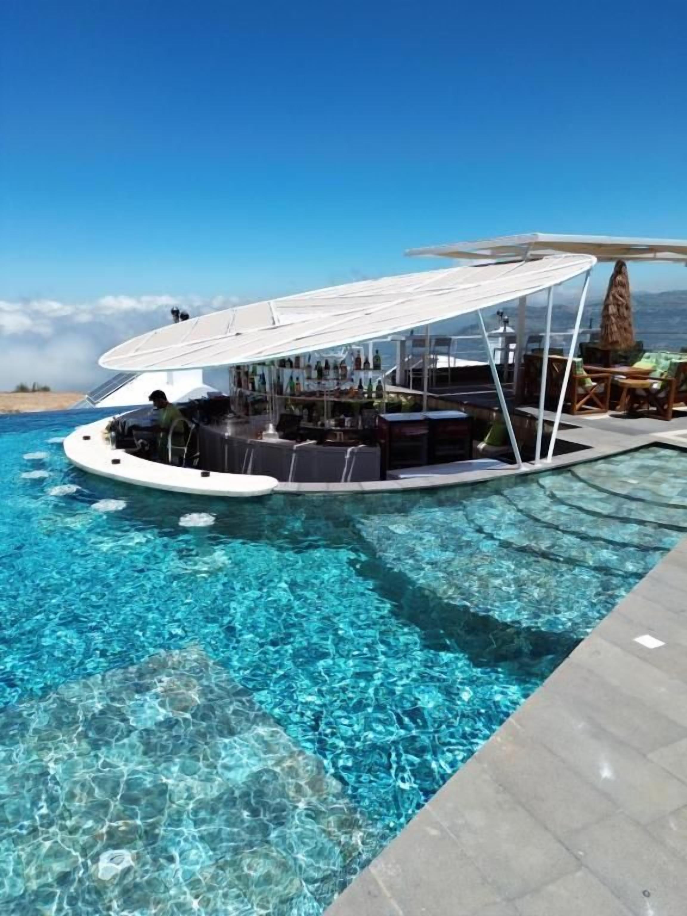 Eine schwimmende Bar mit Pool, umgeben von Liegestühlen und Sonnenschirmen, mit Blick auf das klare, blaue Meer.