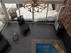 A room with a black leather chair, a small table, a chandelier, and a view of a snowy outdoor area through a glass door. - O Sommet Zaarour (Mchaymcheh)
