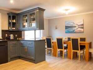 Een moderne keuken met grijze kastjes, een eethoek met houten stoelen en een schilderij aan de muur.
