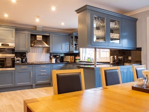 Een moderne keuken met blauwe kastjes, een eethoek met een houten tafel en een inbouwoven.