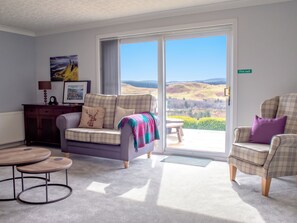A living room with a sofa, armchairs, a coffee table, and a view through a glass door to the outdoors. - Skeabost Bungalow by Interhome (Mid Skye)