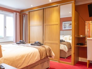 Een hotelkamer met een bed, een kledingkast, een spiegel, een televisie en een raam.