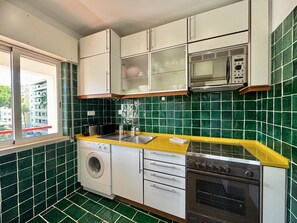 A compact kitchen with a washing machine, a microwave, and an oven. - Vilamoura Golf Apartment 4 by Homing (Loulé)