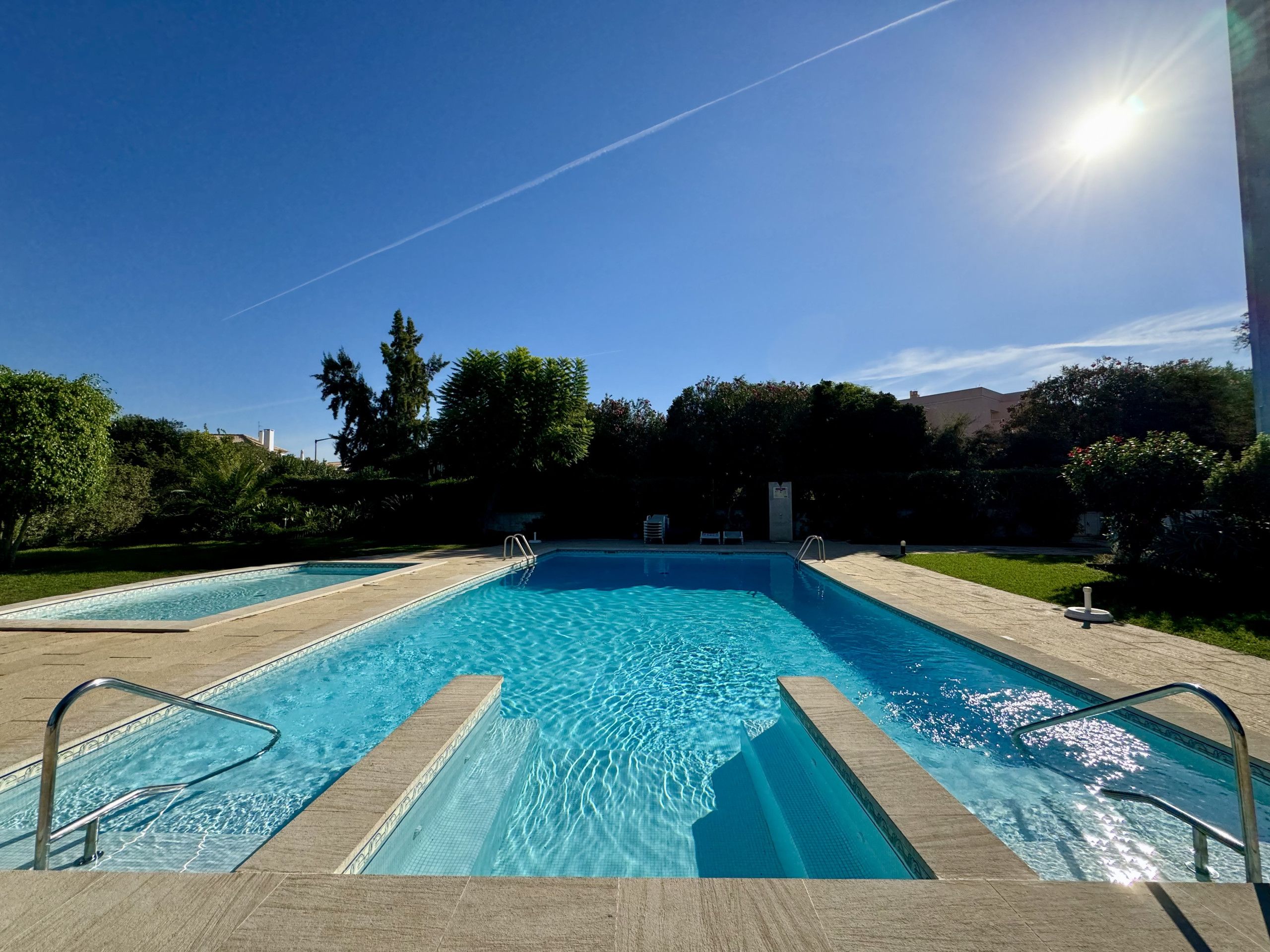 Una piscina rectangular con agua azul cristalina, rodeada por una terraza pavimentada y barandales metálicos.