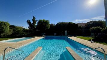 Una piscina rectangular con agua azul cristalina, rodeada por una terraza pavimentada y barandales metálicos.