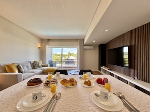 A modern hotel room with a dining area, a sofa, a TV, and a balcony with a view. - Vilamoura Golf Apartment 4 by Homing (Loulé)