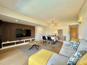Ein modernes Wohnzimmer mit Flachbildfernseher, Essbereich mit Tisch und Stühlen sowie eine Couch mit Zierkissen.