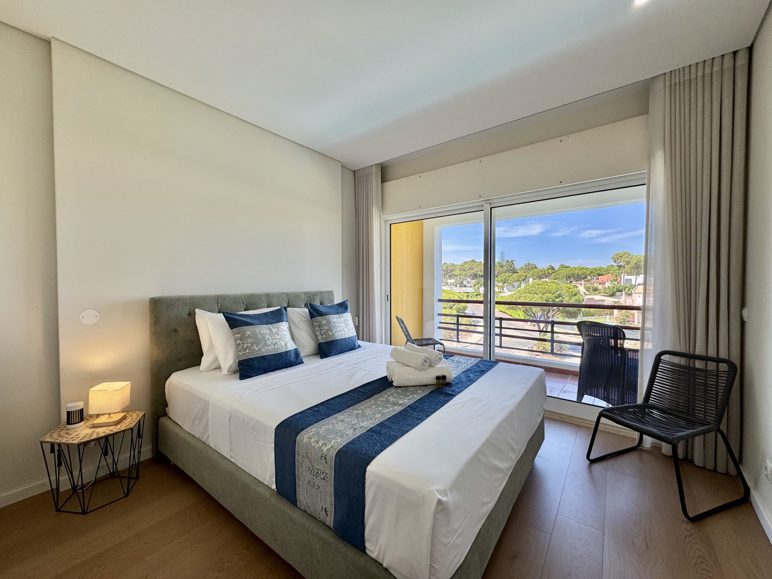 A hotel room with a large bed, a chair, and a balcony with a view.