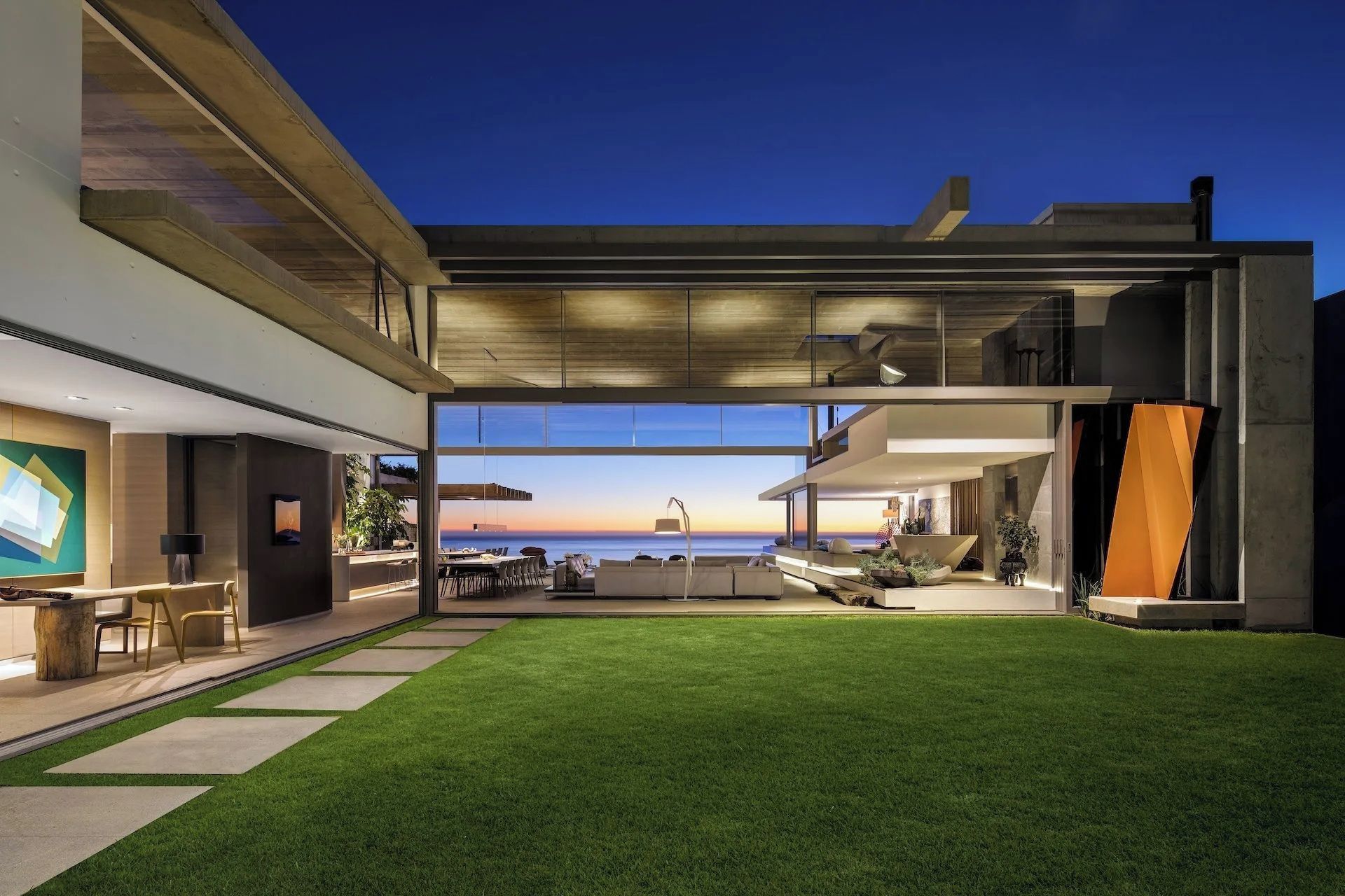 Una casa moderna con un amplio ventanal que da a un patio con vistas al océano.