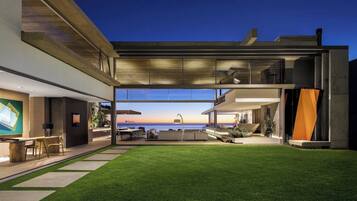 Una casa moderna con un amplio ventanal que da a un patio con vistas al océano.