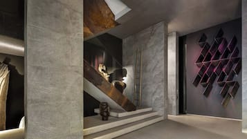 Een modern interieur met een trap, een houten sculptuur en een geometrisch kunstwerk aan de muur.