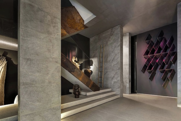 A modern interior with a staircase, a wooden sculpture, and a geometric wall art piece.