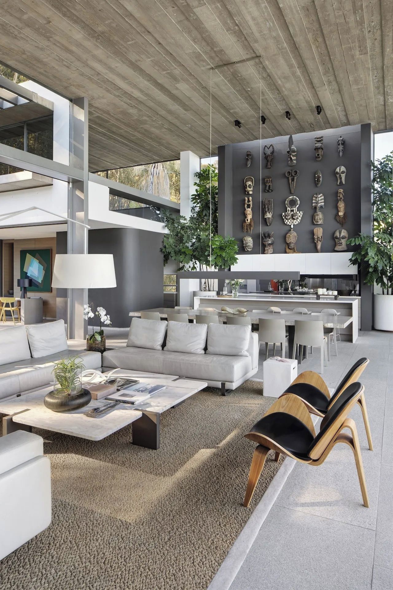 A modern living space with a sofa, coffee table, and chairs, a kitchen area, and a wall with decorative masks.