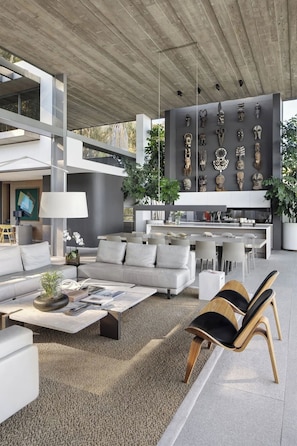 Un espacio de estar moderno con sofá, mesa de centro, sillas, una zona de cocina y una pared decorada con máscaras.