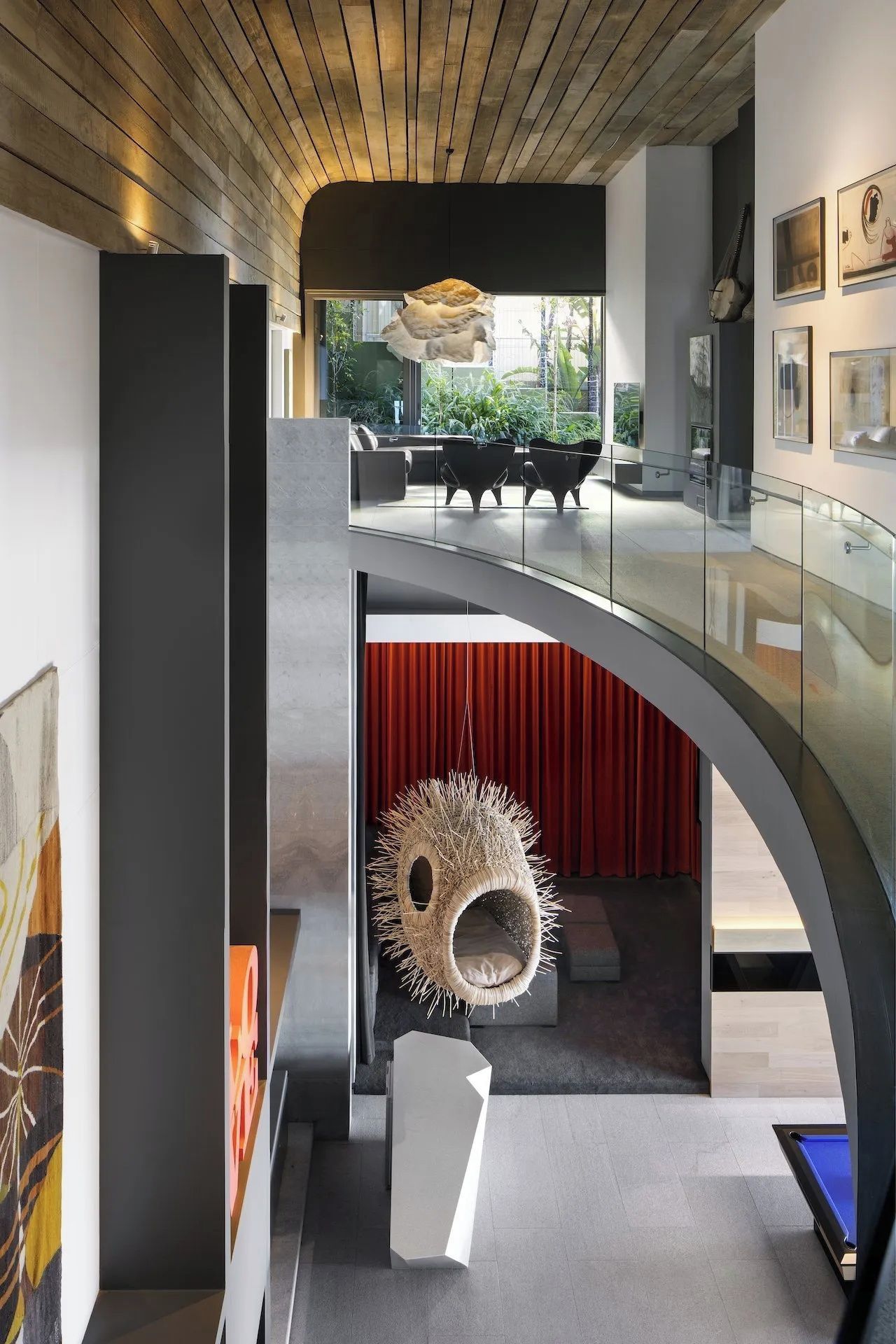 Un interior moderno con barandilla de vidrio curvo, una silla colgante y una escalera que baja a un nivel inferior.