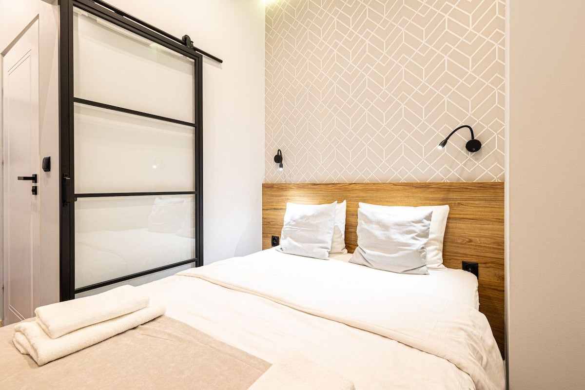 A hotel room with a bed, a wooden headboard, a wall-mounted light fixture, and a sliding door.