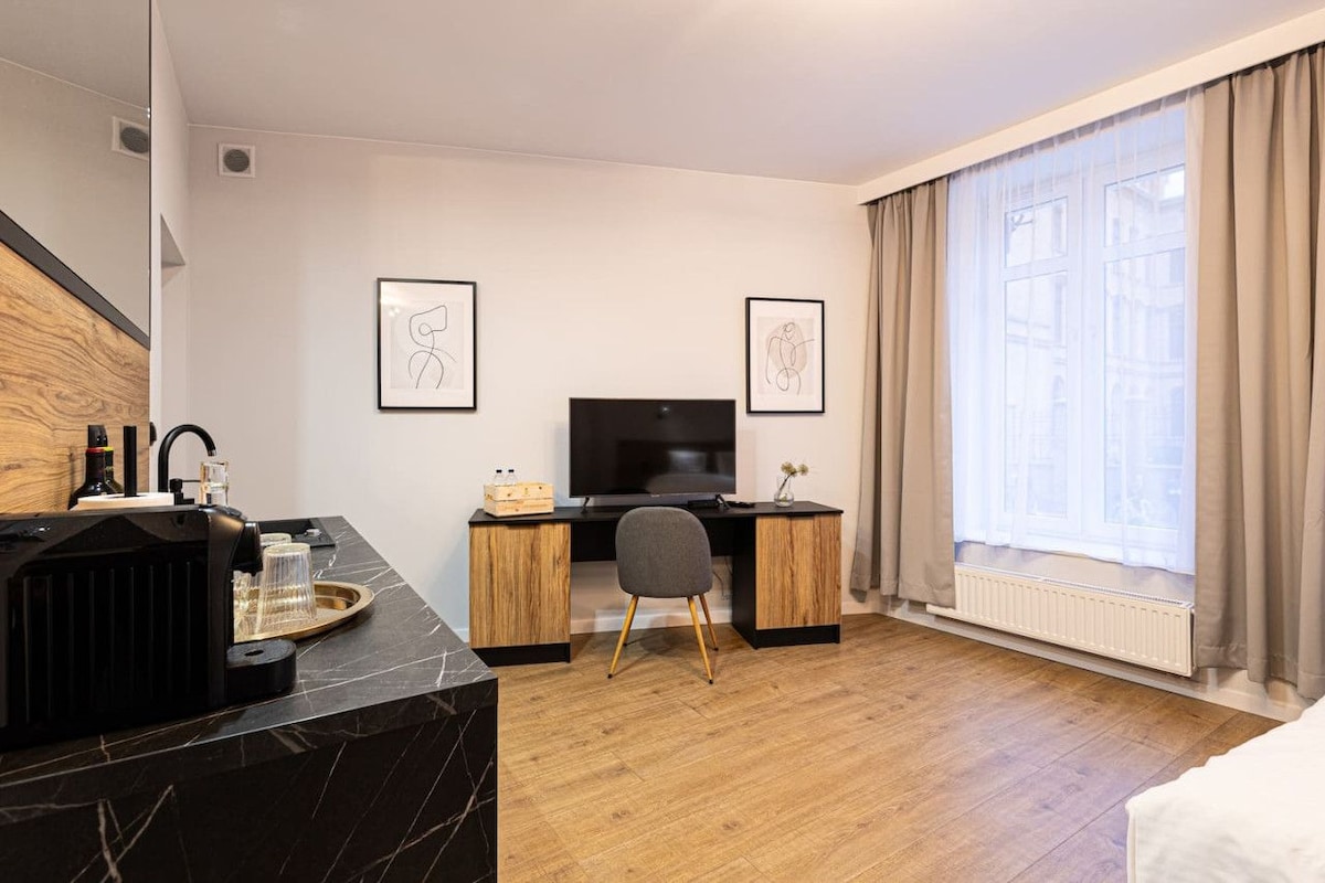 A hotel room with a wooden desk, a television, a chair, a bed, and a window with curtains.